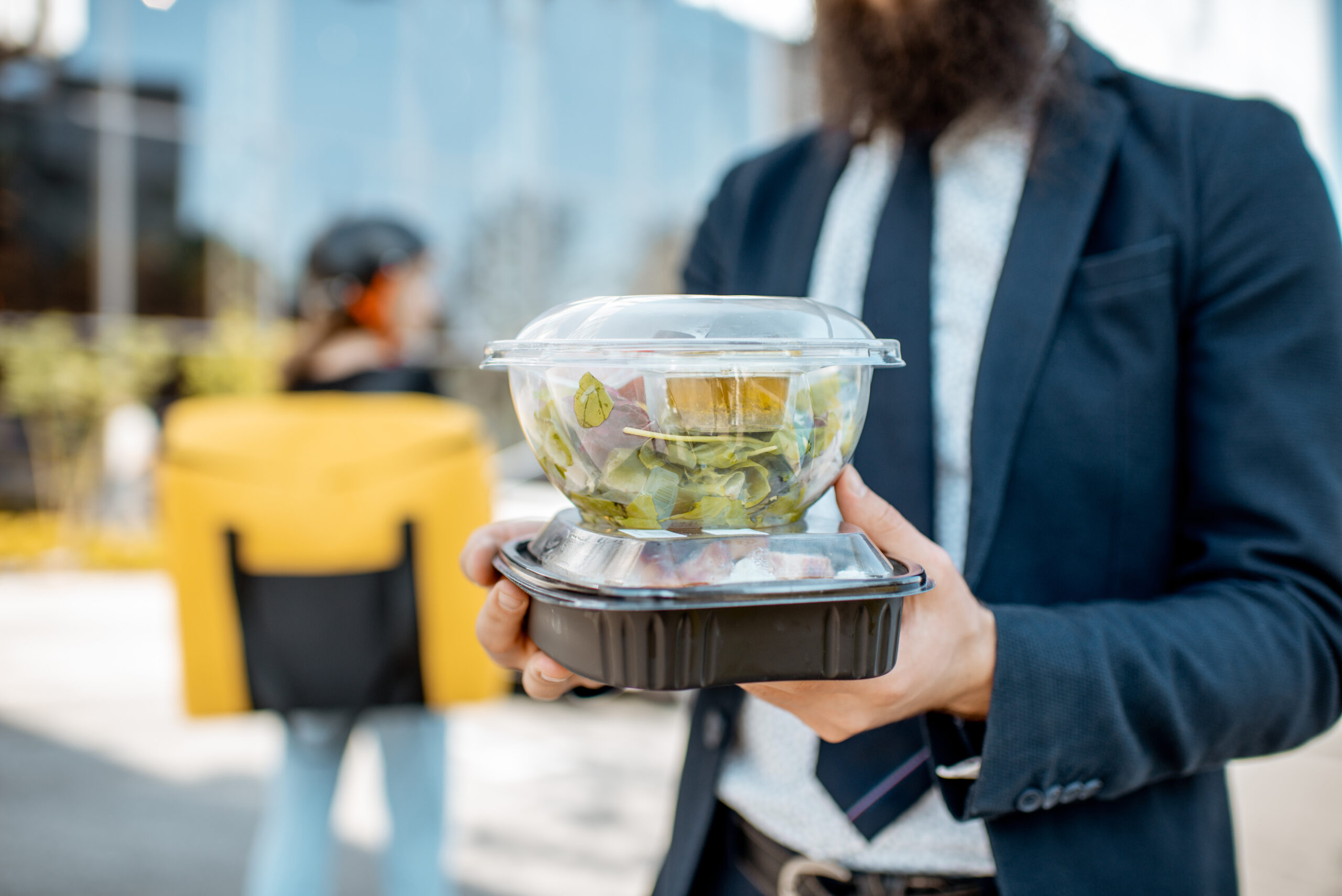 Businessman holding lunch boxes with takeaway food received from a courier outdoors. Food delivery concept